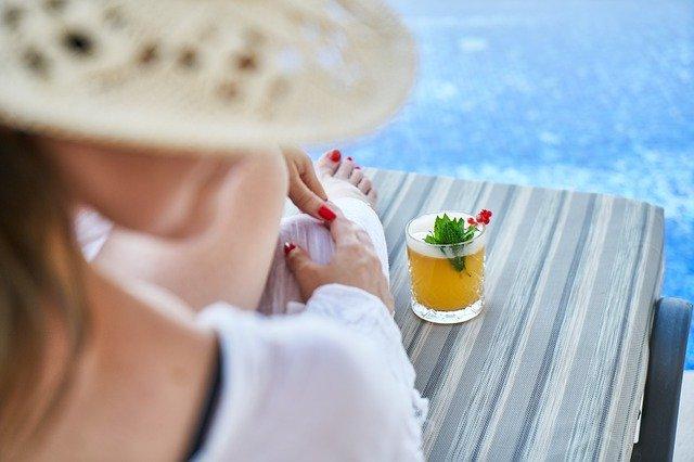 Mujer sentada en una hamaca tomando el sol mientras se toma su bebida fría al lado de la piscina