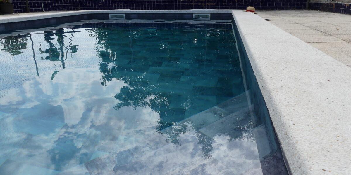 Escalera de obra en una piscina revestida con lámina armada gris, situada en una esquina del vaso.